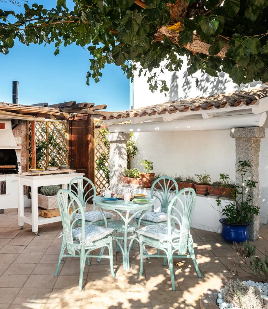 Shaded courtyard of a Sardinian villa, with a table laid under a fig tree beside a whitewashed loggia
