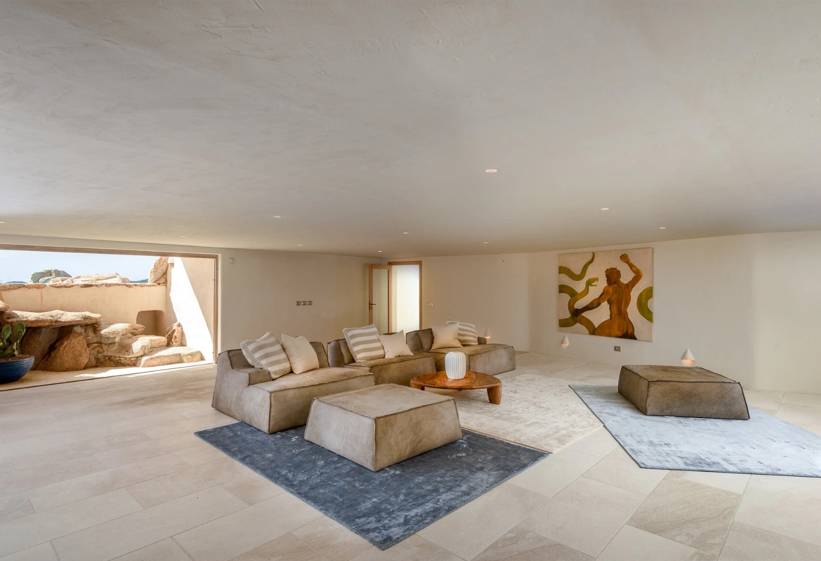 Living room of a luxury villa in Sardinia, with plaster walls, low sofas and an opening onto a granite courtyard
